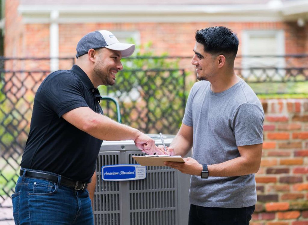 AC technician with a client in front of an american standard hvac unit